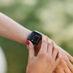 Mujer joven sonriendo mientras consulta una app de salud con IA en su smartphone y lleva un smartwatch, mostrando el monitore