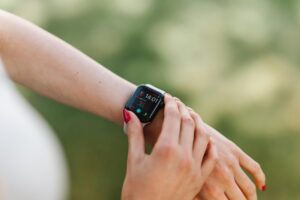 Mujer joven sonriendo mientras consulta una app de salud con IA en su smartphone y lleva un smartwatch, mostrando el monitore
