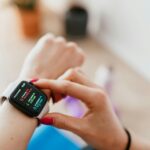 Una mujer joven con una sonrisa serena consulta una aplicación de salud en su smartwatch mientras realiza ejercicio suave al