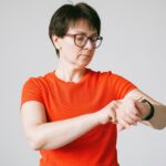 Una mujer de mediana edad sonríe mientras revisa sus datos de salud en una aplicación móvil, con un smartwatch moderno visibl