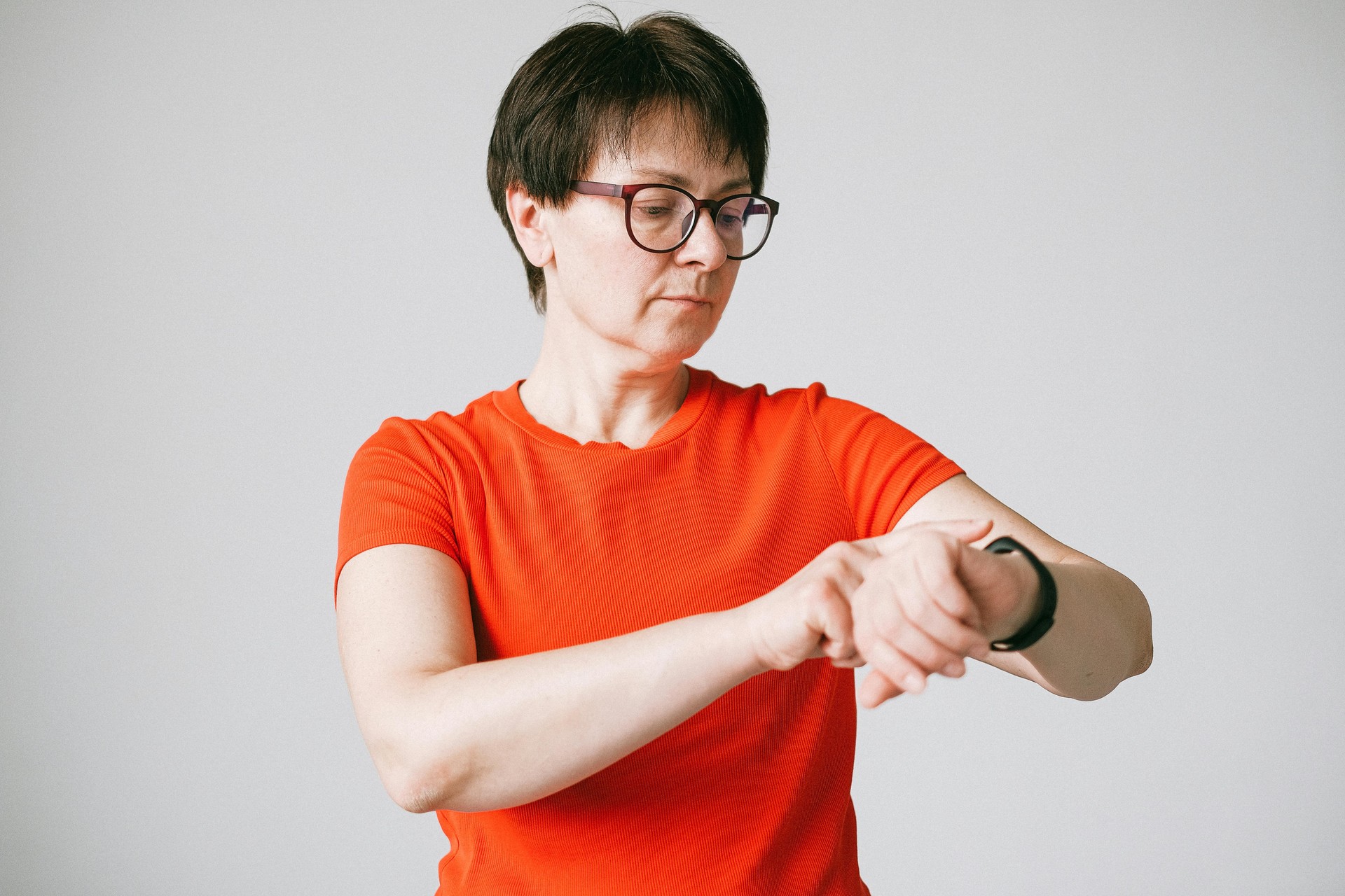 Una mujer de mediana edad sonríe mientras revisa sus datos de salud en una aplicación móvil, con un smartwatch moderno visibl