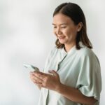 Una mujer joven sonriendo mientras interactúa con una aplicación de asistente de salud digital con IA en su smartphone, que m