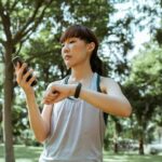 Una mujer sonriente de mediana edad interactuando con una aplicación de salud en su smartphone, que muestra gráficos de activ