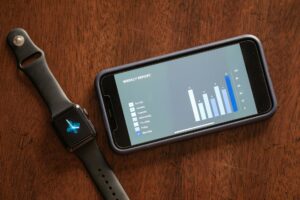 Mujer joven revisando datos de salud en su smartphone, mostrando gráficos de un smartwatch, simbolizando la IA para la preven