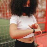 Mujer joven revisando datos de salud en su smartwatch y smartphone, con gráficos de IA. Ilustra la IA en salud preventiva.