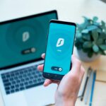 Una persona joven mirando la pantalla de un smartphone con iconos de candado y escudo superpuestos, simbolizando la protecció