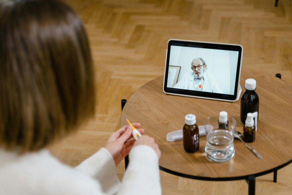Médico sonriente se comunica por videollamada con un paciente desde su consulta, mostrando tecnología de salud digital.