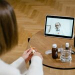 Médico sonriente se comunica por videollamada con un paciente desde su consulta, mostrando tecnología de salud digital.
