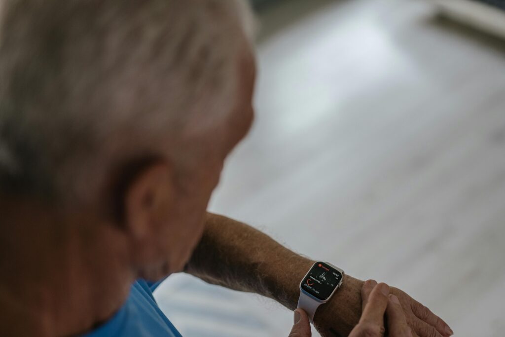 Persona mayor sonriente revisando datos de salud en un smartwatch en casa, simbolizando el monitoreo de enfermedades crónicas
