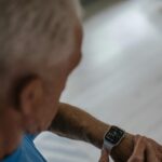 Persona mayor sonriente revisando datos de salud en un smartwatch en casa, simbolizando el monitoreo de enfermedades crónicas