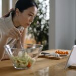 Mujer sonriente usando una tablet para consultar una app de nutrición personalizada, con frutas y verduras frescas sobre la m
